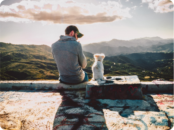 A man and his dog sitting on ledge overlooking mountains